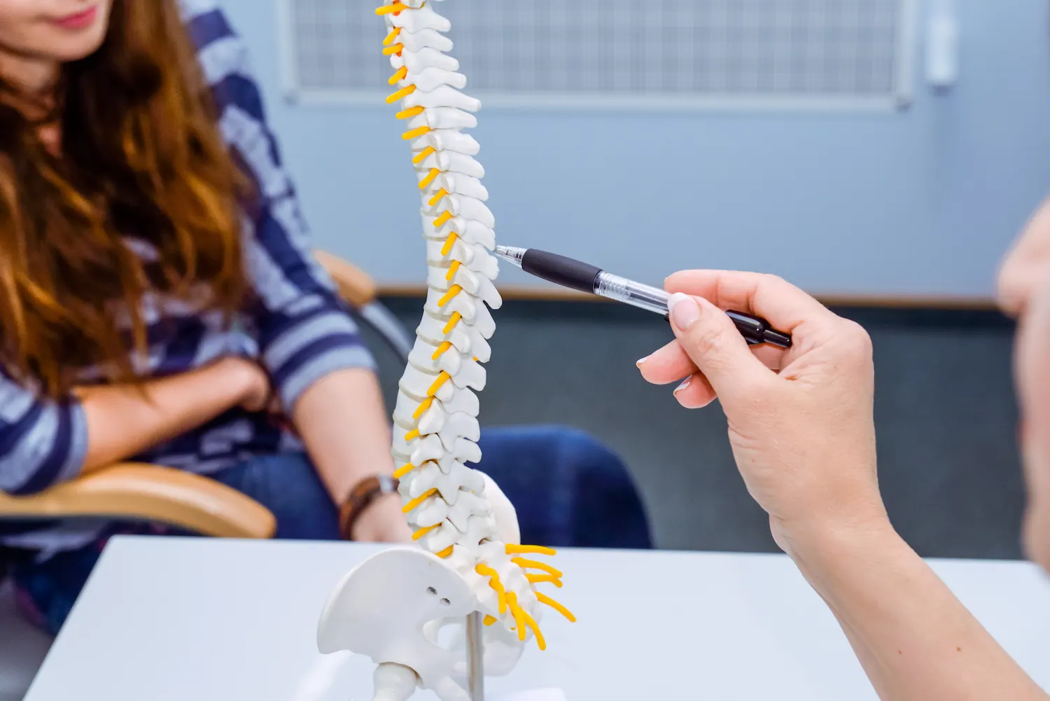 Chiropractor pointing to a spine model while explaining a patient’s problem